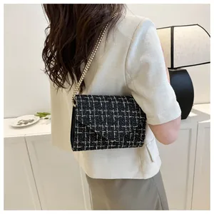 Primer plano de un bolso de cadena en tweed blanco y negro colgado al hombro en un interior