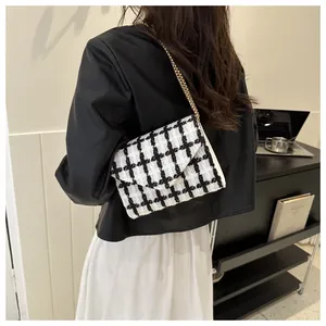 Bolso bandolera de tweed blanco y negro con cadena dorada mostrado al hombro en modelo