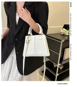 Primer plano de bolso blanco con textura de cocodrilo, herrajes dorados y correa fina