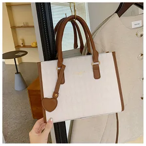 Macro shot of white diamond-patterned tote bag with brown handles and heart charm accessory
