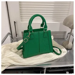 Detalle del bolso verde lima con textura de cocodrilo y herrajes dorados sobre blanco