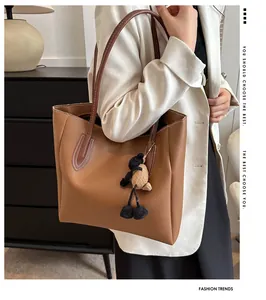 Detail of brown leather tote bag with white stitching and cute bear charm accessory