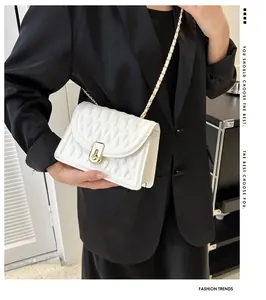Detail of white quilted crossbody bag with gold chain strap and lock on black blazer