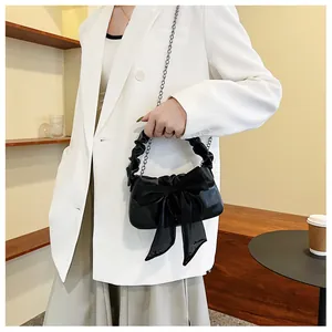 Primo piano di borsa nera con fiocco in velo e manico arricciato su blazer bianco