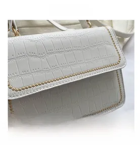 Detail of white crocodile embossed leather bag with yellow wavy embroidery and gold buckle