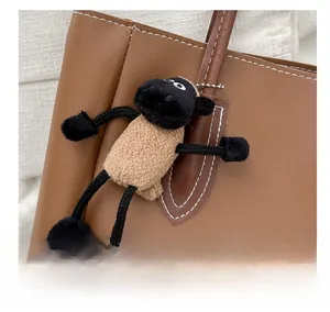 Close-up of fluffy black-faced sheep plush charm hanging on a brown leather tote bag