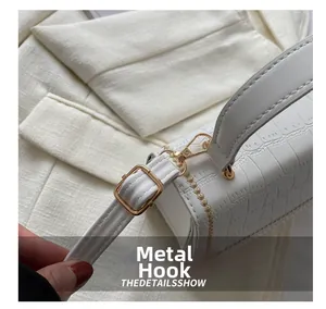 Close-up of golden metal hook and crocodile texture leather strap on white handbag