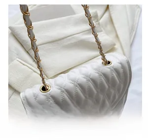 Detail of white quilted crossbody bag featuring metal chain strap and luxury stitching