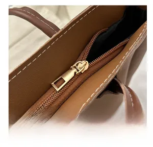 Macro shot of smooth gold metal zipper and white contrast stitching on a brown leather tote bag