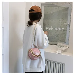 Close-up of pink round basketball purse with gold chain strap on a model with white hoodie