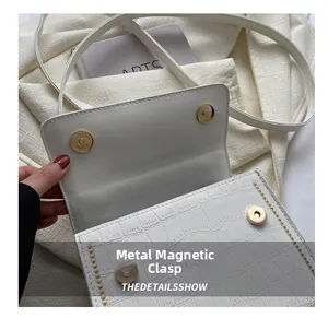 Detail of magnetic buckle closures on crocodile texture white crossbody bag