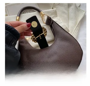 Close-up of golden piston magnetic clasp on dark brown litchi pattern leather handbag