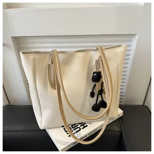 Detail of a beige tote bag with brown straps and a cute sheep plush charm on a book