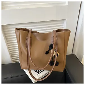 Detail of a brown leather tote bag with white stitching and a cute sheep plush charm