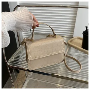 Detail of cream crocodile embossed handbag featuring golden bead rivets and top handle