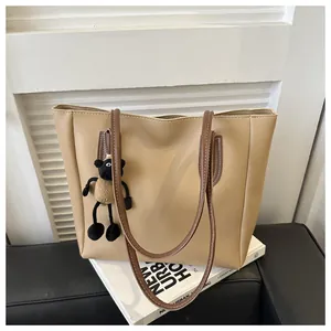 Close-up of khaki tote bag with a plush sheep charm on white books and black surface