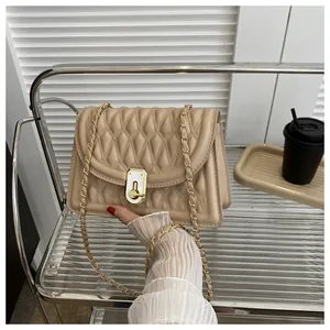 Close-up of beige quilted crossbody bag with gold chain strap and metal lock detail