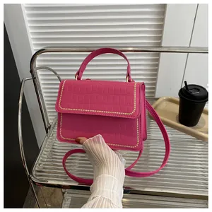 Close-up of rose red handbag with crocodile pattern texture and gold rivet detailing
