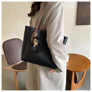 Detail of black tote bag with brown straps, contrast stitching, and plush alpaca charm