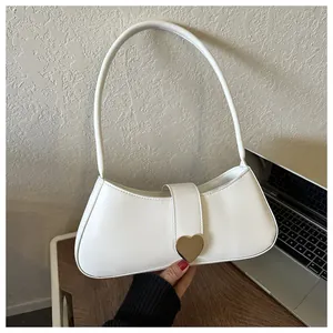 Detailed macro view of the gold heart-shaped buckle on a white leather underarm handbag