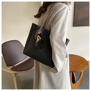 Detail of black tote bag with white stitching, brown strap and sheep charm on a model