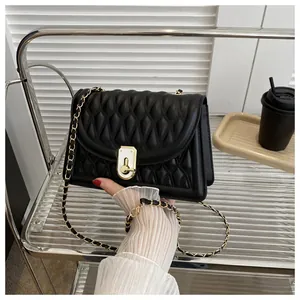 Detail of black quilted leather bag with gold chain and unique metal lock on a shelf