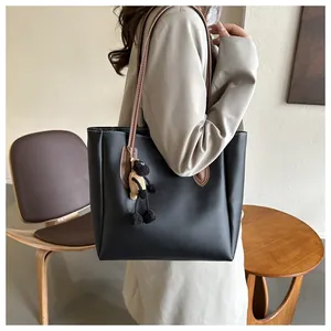 Detail of black tote bag featuring brown straps and a small plush sheep pendant