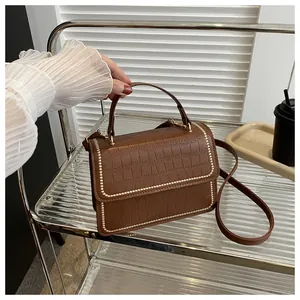 Detail of dark brown crocodile texture handbag with elegant gold beaded trim and handle