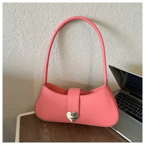Detail of pink faux leather baguette bag featuring a large silver heart buckle on a desk