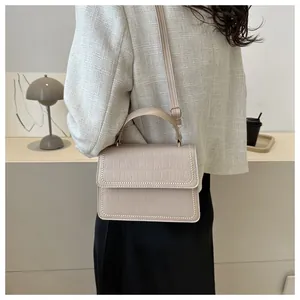 Detail showing the beige crocodile embossed leather texture and gold stud trim on the bag