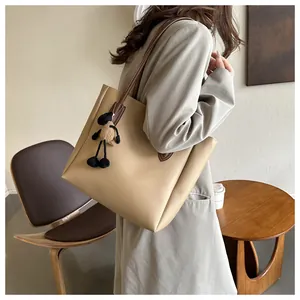 Large khaki tote bag with plush charm shown worn by a model in a cozy cafe setting