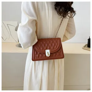 Detail of reddish-brown quilted shoulder bag with metal chain strap on model