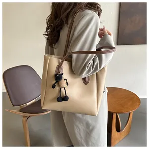 Detail of a large beige leather tote bag with brown straps and a small sheep charm