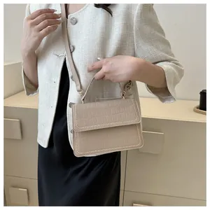 Detail of beige crocodile embossed small square bag with decorative gold rivets on handle