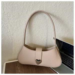 Detailed view of beige baguette bag with large gold heart buckle on a wooden desk