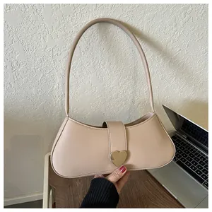 Detail of minimalist beige underarm bag featuring a delicate golden heart-shaped metal clasp