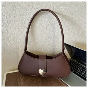 Close-up of matte brown faux leather underarm bag featuring a silver heart-shaped buckle