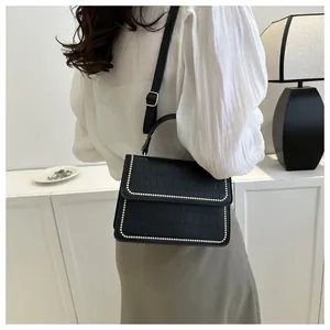 Detail of black crocodile texture handbag with beaded edge worn by a model
