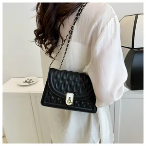 Detailed view of black quilted crossbody bag with gold chain strap on a model shoulder