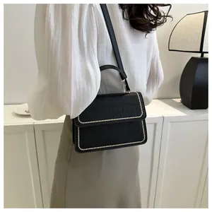Close-up of black crocodile-embossed shoulder bag with elegant golden bead detailing