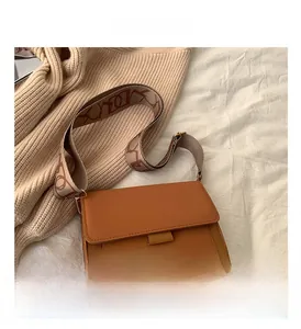 Detail view of brown square crossbody bag with a wide patterned strap on a textured background