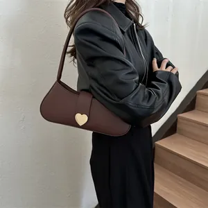 Minimalist dark brown leather underarm bag featuring a large gold heart buckle