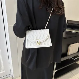 White quilted chain crossbody bag with gold lock shown on a model in a minimal setting