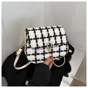 Detail of tweed crossbody bag featuring a golden horseshoe buckle and white leather side