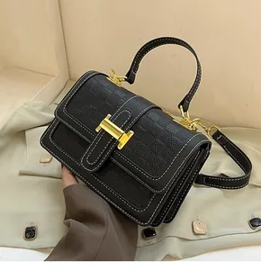 Detailed view of black pebbled leather handbag with gold H buckle and contrast stitching
