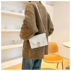 Detail of white envelope crossbody bag with a gold water drop twist lock and PU leather texture