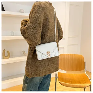 Side view of a white leather crossbody bag with triangular gold metal clasp on a model