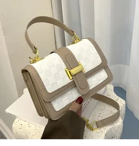 Detail of white checkered flap bag featuring gold hardware and khaki leather shoulder strap