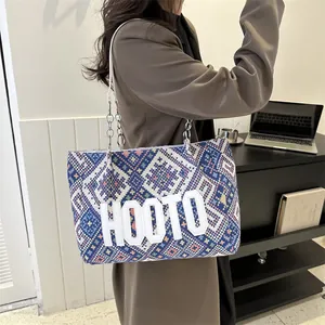 Ethnic style geometric tote bag with blue patterns and silver chain strap on a model