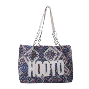Ethnic style tote bag with geometric pattern weave and metal chain handle on white background